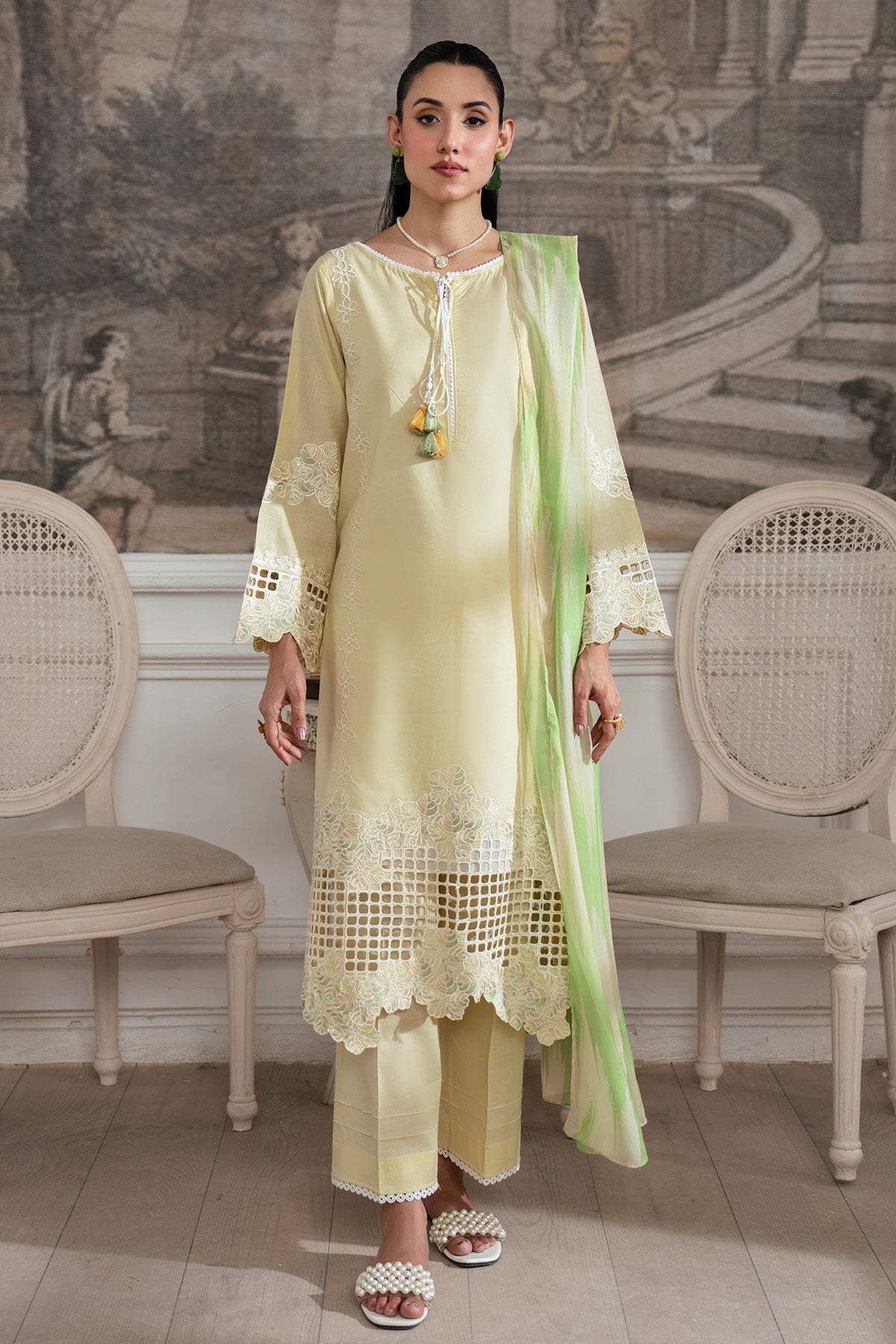Woman in a light yellow traditional outfit with a green dupatta in an elegant room.