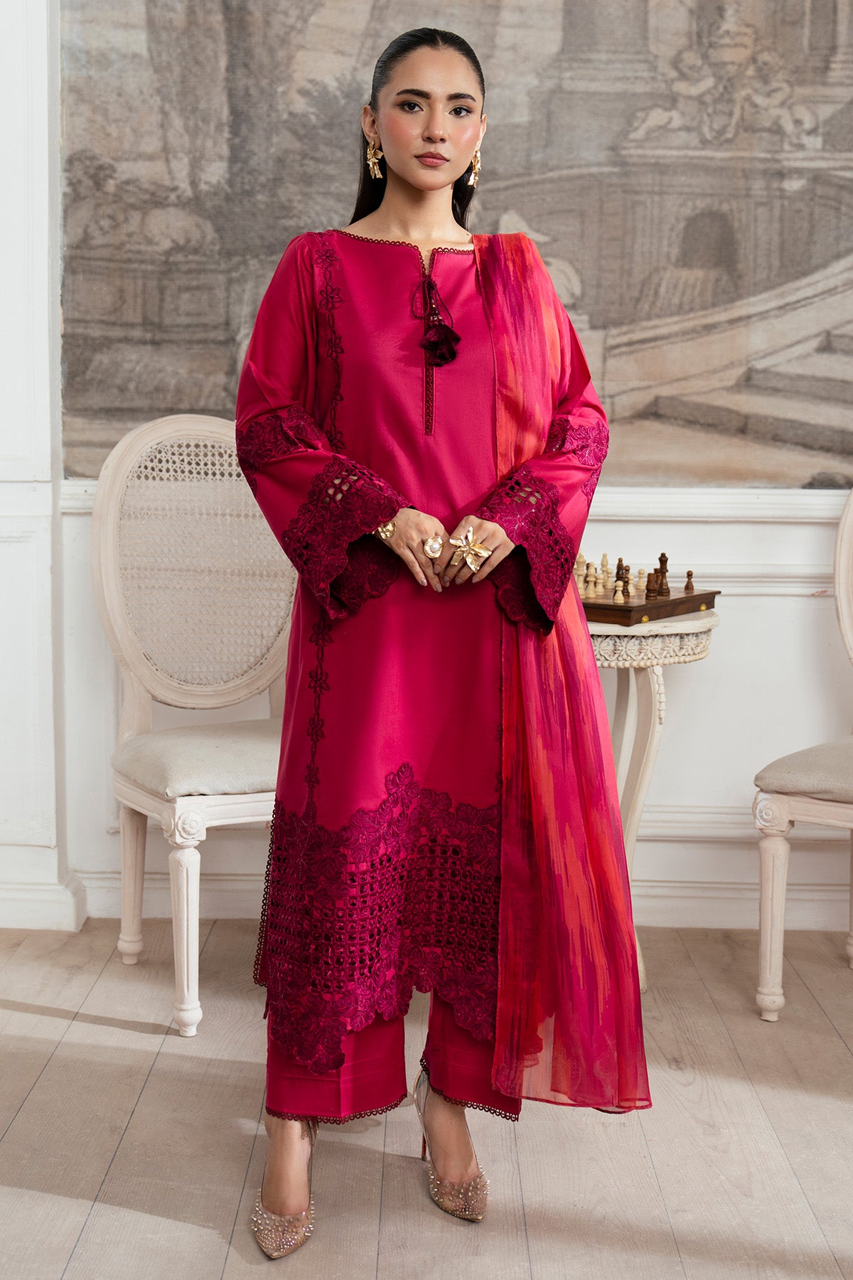 Woman in a red traditional outfit standing in an elegant room with classical decor.