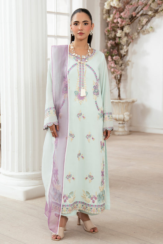 Woman in a light green embroidered dress with a floral pattern in a decorated room.