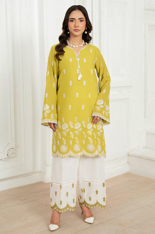 Woman wearing a yellow and white embroidered outfit in a room with white curtains.