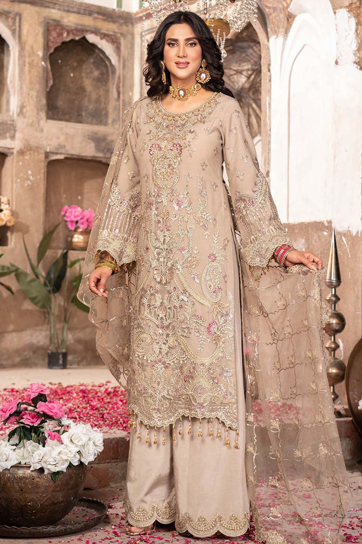 Woman in a beige embroidered traditional outfit standing in an ornate indoor setting.