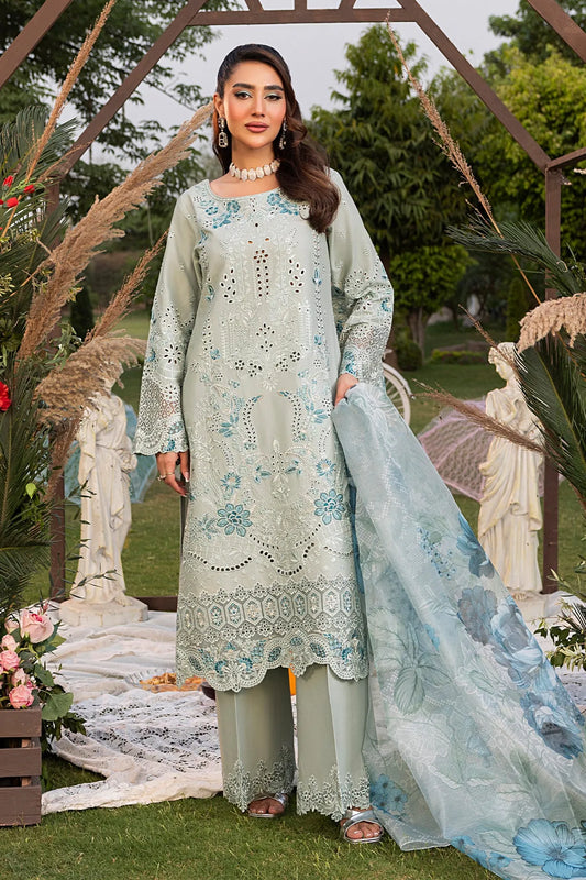A woman wearing a traditional green dress with intricate embroidery, accompanied by a light blue dupatta with artistic prints, and standing in a garden setting.